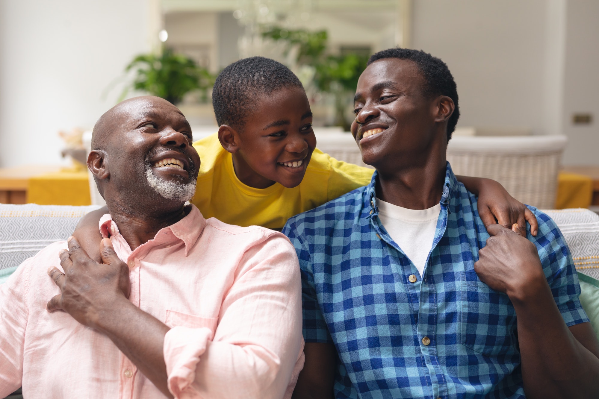 Happy african american boy with father and grandfather sitting on sofa at home