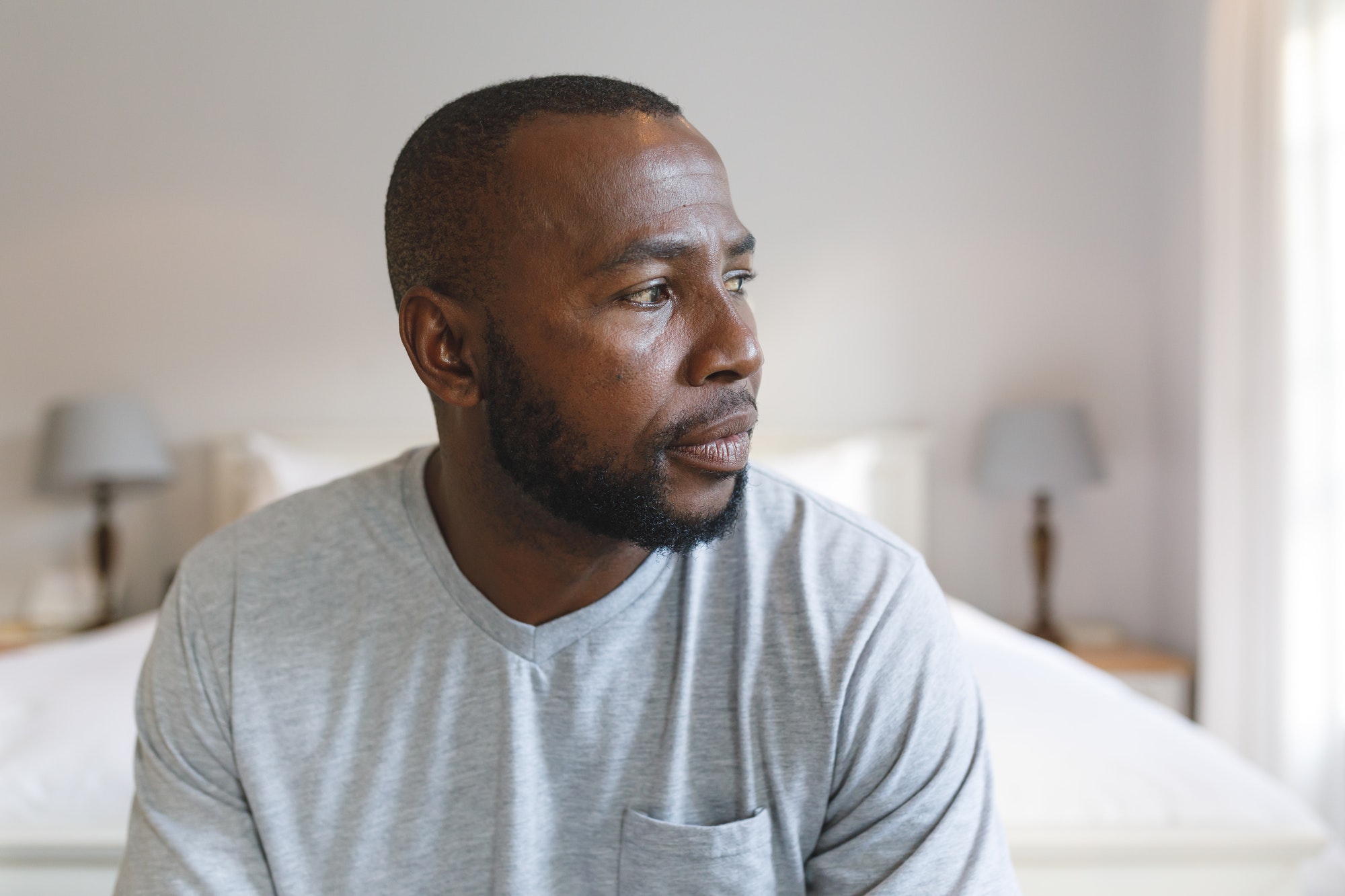 Thoughtful african american man sitting on bed and looking away in bedroom